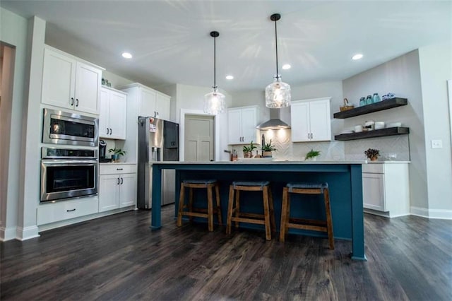 kitchen featuring decorative light fixtures, white cabinets, stainless steel appliances, and a center island with sink