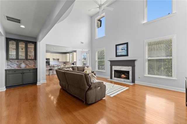 living room featuring a premium fireplace, hardwood / wood-style floors, ceiling fan, and a high ceiling