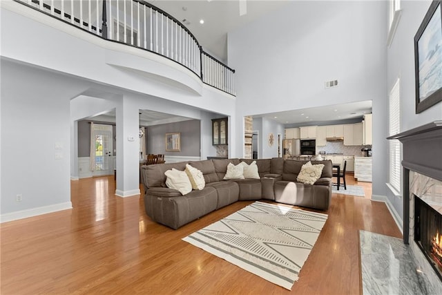 living room featuring a towering ceiling, a high end fireplace, and light wood-type flooring