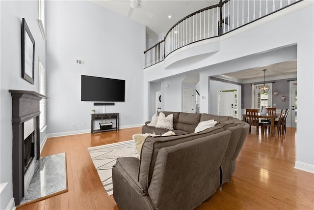 living room featuring light hardwood / wood-style flooring, a towering ceiling, and ceiling fan with notable chandelier