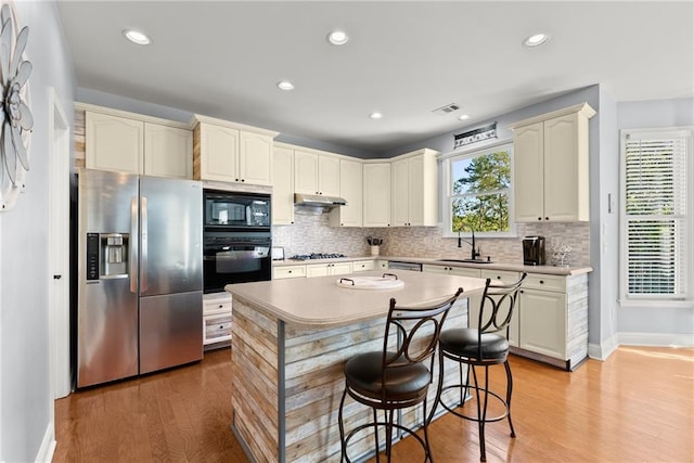 kitchen featuring black appliances, sink, decorative backsplash, light wood-type flooring, and a breakfast bar area