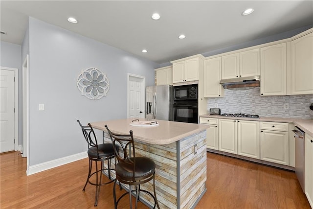 kitchen with a center island, backsplash, black appliances, light hardwood / wood-style flooring, and a kitchen bar