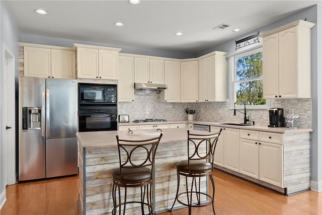 kitchen featuring a center island, black appliances, sink, tasteful backsplash, and light hardwood / wood-style floors