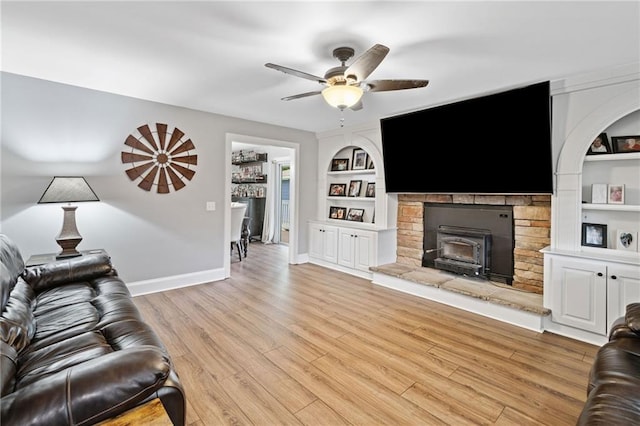 2545 Hickory Level Rd, Villa Rica, GA 30180 - living room featuring built in shelves, baseboards, ceiling fan, light wood-type flooring, and a stone fireplace