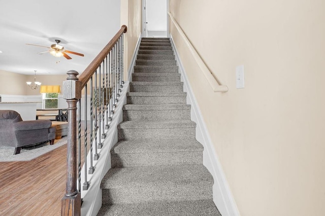 stairway featuring carpet and ceiling fan with notable chandelier