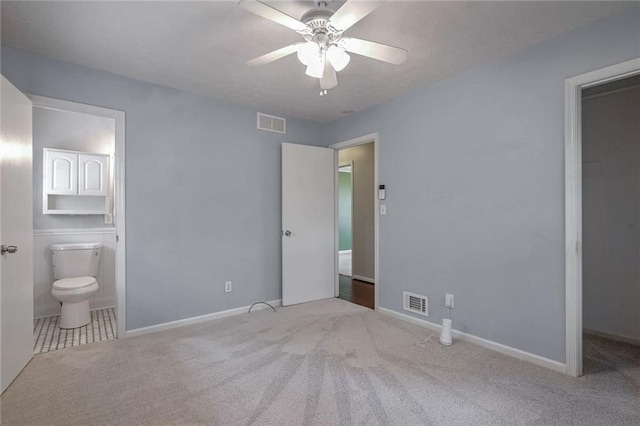 unfurnished bedroom featuring a walk in closet, light colored carpet, ensuite bath, and ceiling fan