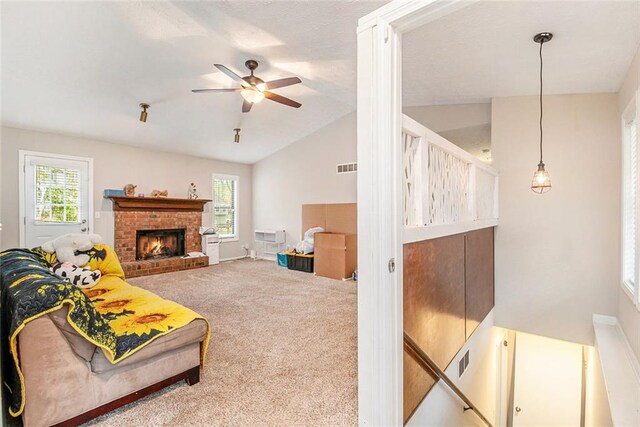 carpeted living room featuring a brick fireplace, visible vents, vaulted ceiling, and ceiling fan