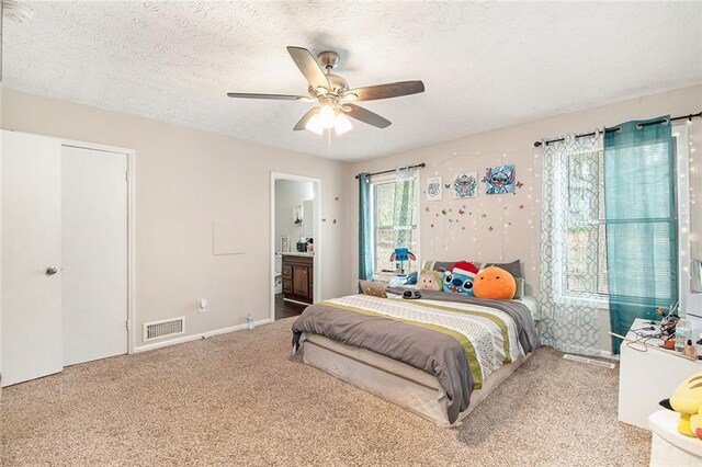 carpeted bedroom with a textured ceiling, visible vents, a ceiling fan, and connected bathroom