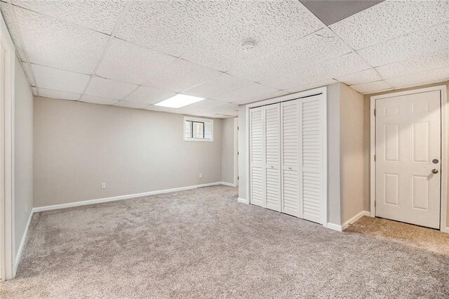 unfurnished bedroom featuring a drop ceiling, carpet, a closet, and baseboards