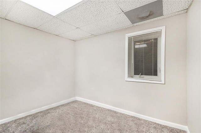 carpeted spare room with a drop ceiling and baseboards