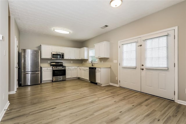kitchen with appliances with stainless steel finishes, light wood-style floors, baseboards, and white cabinetry