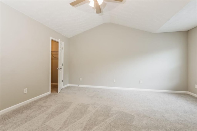 unfurnished bedroom with light colored carpet, lofted ceiling, baseboards, a walk in closet, and ceiling fan