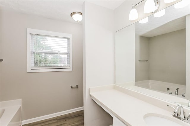 bathroom with a bath, a sink, wood finished floors, and baseboards