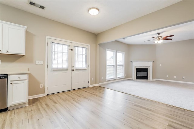 unfurnished living room featuring light wood finished floors, a fireplace with flush hearth, baseboards, a ceiling fan, and french doors