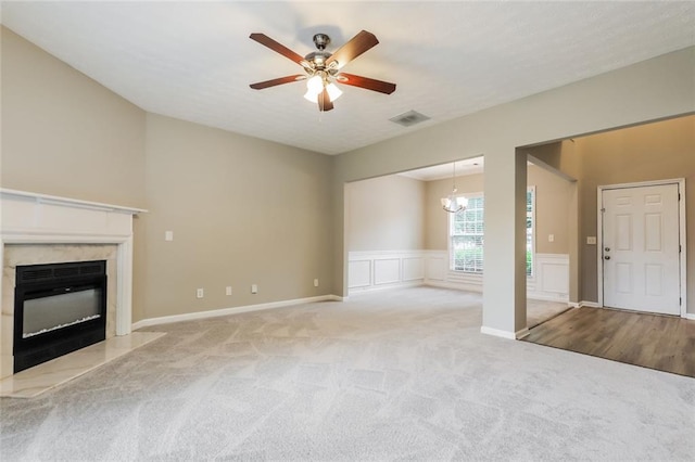 unfurnished living room featuring a premium fireplace, carpet floors, ceiling fan, a chandelier, and wainscoting