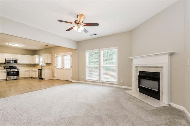 unfurnished living room featuring light colored carpet, a ceiling fan, baseboards, and a high end fireplace