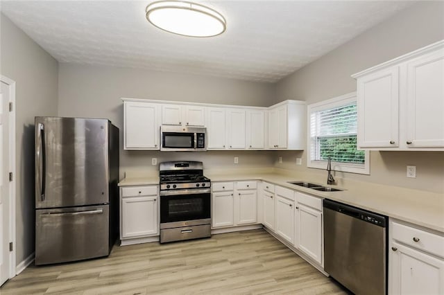 kitchen featuring stainless steel appliances, a sink, light wood-type flooring, white cabinets, and light countertops