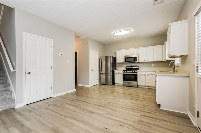 kitchen with stainless steel appliances, light wood-style flooring, light countertops, baseboards, and a textured ceiling