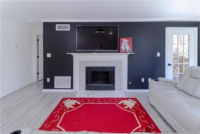 living room featuring crown molding, wood-type flooring, and a tiled fireplace