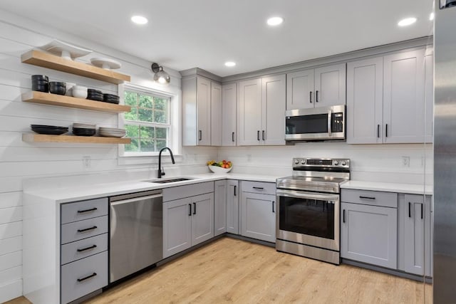 kitchen featuring stainless steel appliances, gray cabinets, a sink, light countertops, and light wood finished floors