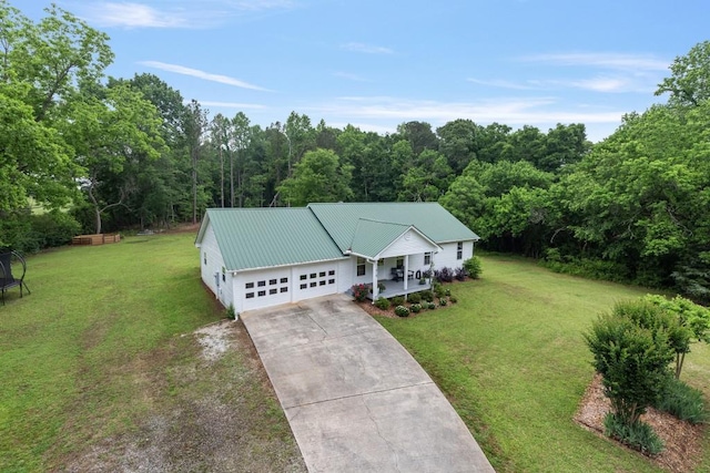 view of front of home featuring an attached garage, concrete driveway, a front lawn, covered porch, and metal roof