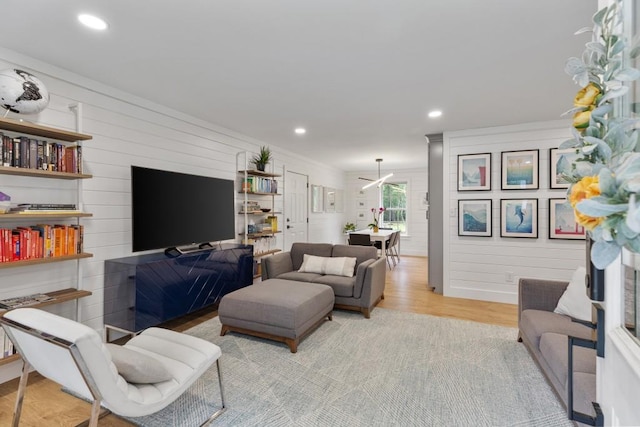 living room featuring light wood-style floors, recessed lighting, wooden walls, and ornamental molding