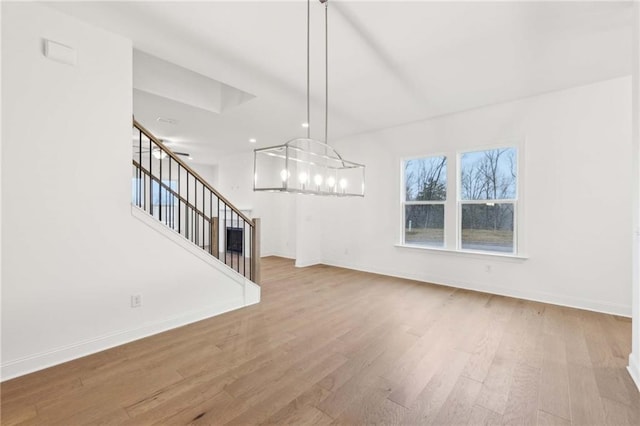 unfurnished living room featuring baseboards, stairway, a chandelier, and wood finished floors