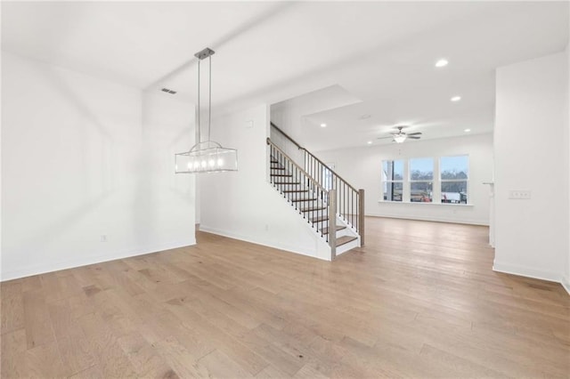 unfurnished living room featuring ceiling fan with notable chandelier, light wood-type flooring, recessed lighting, stairway, and baseboards