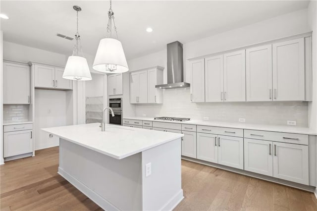 kitchen with light countertops, visible vents, wall chimney exhaust hood, appliances with stainless steel finishes, and light wood finished floors