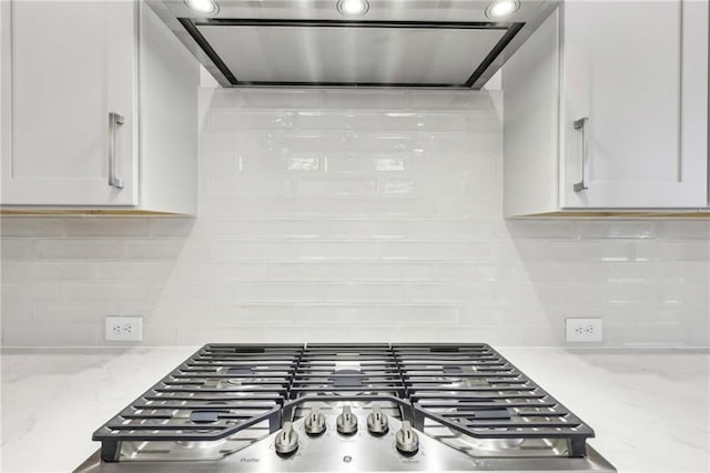 kitchen with tasteful backsplash, range hood, white cabinetry, stainless steel gas cooktop, and light stone counters