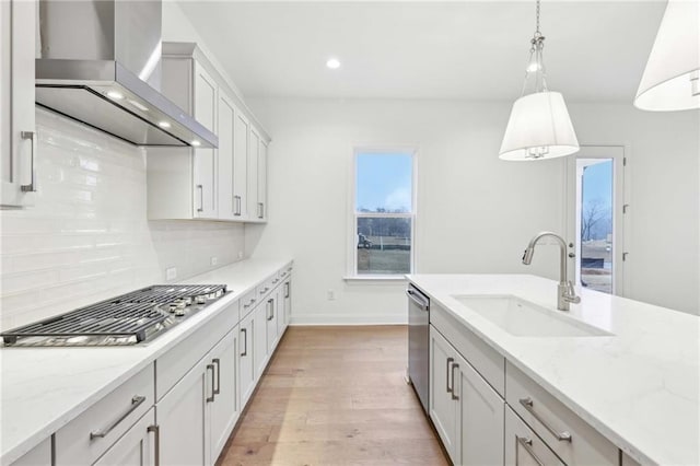 kitchen with light wood-type flooring, wall chimney exhaust hood, stainless steel appliances, pendant lighting, and a sink