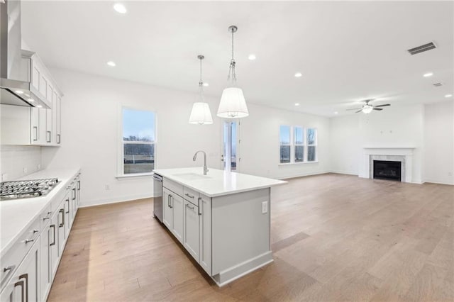 kitchen with wall chimney exhaust hood, light countertops, ceiling fan, appliances with stainless steel finishes, and light wood-style floors