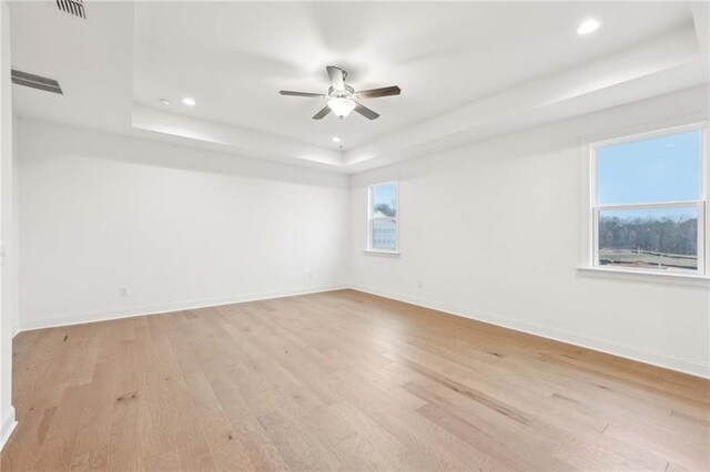 spare room featuring a tray ceiling, light wood-type flooring, ceiling fan, and baseboards