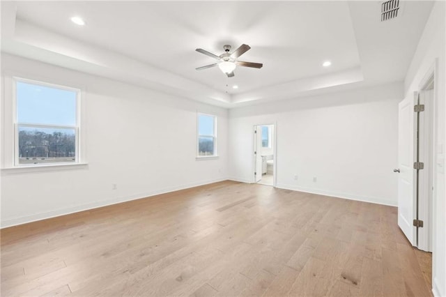 unfurnished room featuring baseboards, visible vents, a tray ceiling, ceiling fan, and light wood finished floors