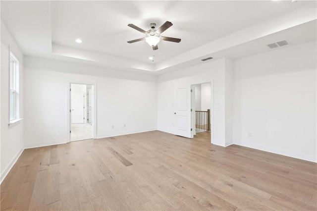 empty room with visible vents, baseboards, ceiling fan, a tray ceiling, and light wood-style flooring