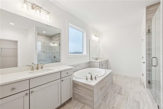 bathroom with two vanities, a stall shower, a walk in closet, a bath, and a sink