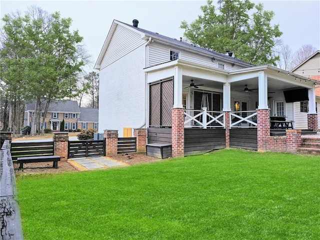 rear view of property featuring a gate, a ceiling fan, fence, a yard, and brick siding