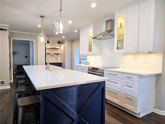 kitchen featuring stainless steel electric stove, an island with sink, a sink, crown molding, and wall chimney exhaust hood