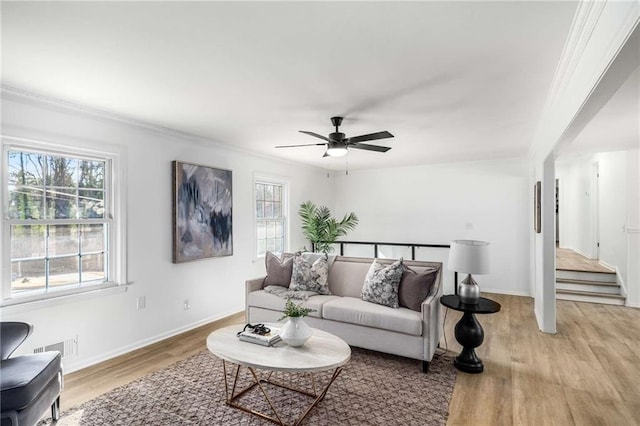 living room with light wood-style floors, a ceiling fan, ornamental molding, baseboards, and stairs