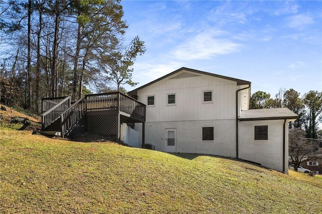 rear view of property with stairway, a deck, a lawn, and brick siding