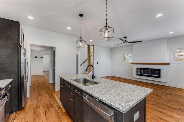 kitchen featuring stainless steel appliances, a glass covered fireplace, a sink, and light wood-style floors