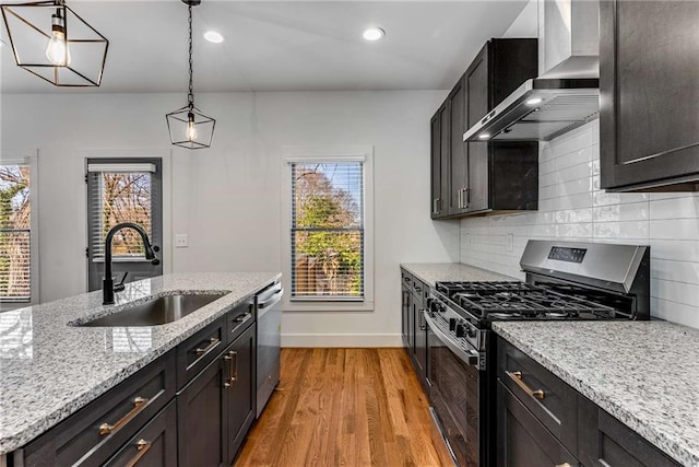 kitchen with a sink, appliances with stainless steel finishes, wall chimney range hood, backsplash, and light wood finished floors