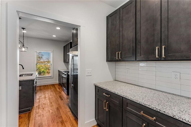 kitchen with light stone counters, a sink, baseboards, light wood-type flooring, and decorative backsplash