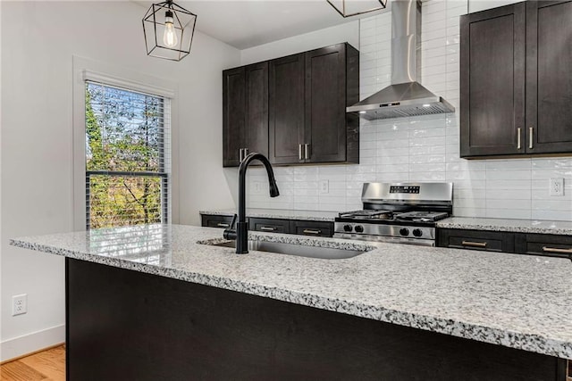 kitchen featuring light wood-style flooring, decorative backsplash, a sink, stainless steel gas range oven, and wall chimney exhaust hood