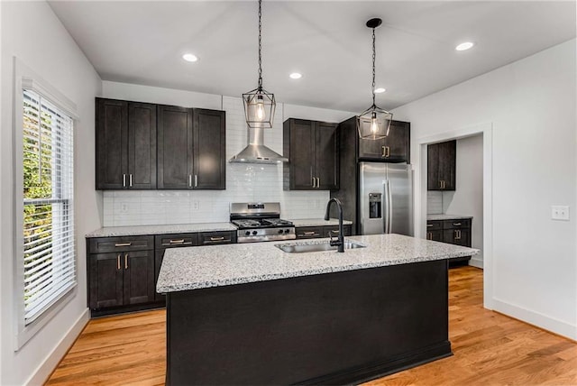 kitchen with light wood finished floors, wall chimney exhaust hood, appliances with stainless steel finishes, and a sink