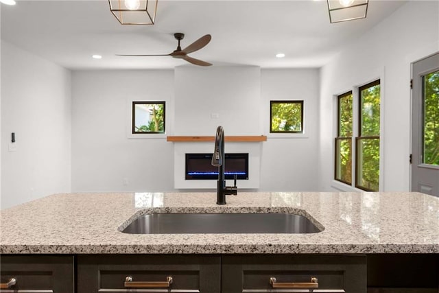 kitchen with a glass covered fireplace, open floor plan, a sink, and light stone countertops