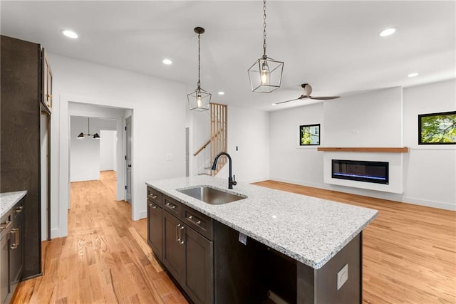 kitchen with light wood-type flooring, dark brown cabinets, a sink, and a glass covered fireplace