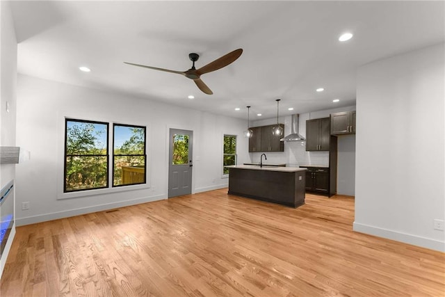 kitchen with light wood finished floors, light countertops, wall chimney range hood, a sink, and recessed lighting