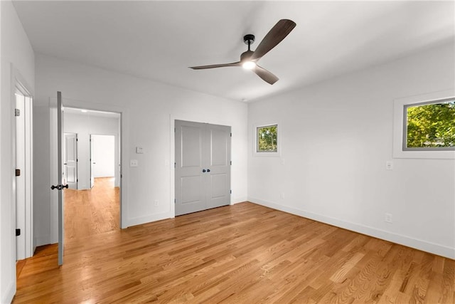 unfurnished bedroom featuring a ceiling fan, baseboards, multiple windows, and light wood finished floors