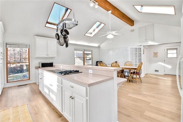 kitchen featuring white cabinetry, stainless steel gas cooktop, ceiling fan, light wood-type flooring, and lofted ceiling with skylight